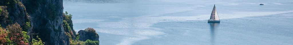 Vitorlás yacht a nyugodt kék tengeren, sziklás part közelében